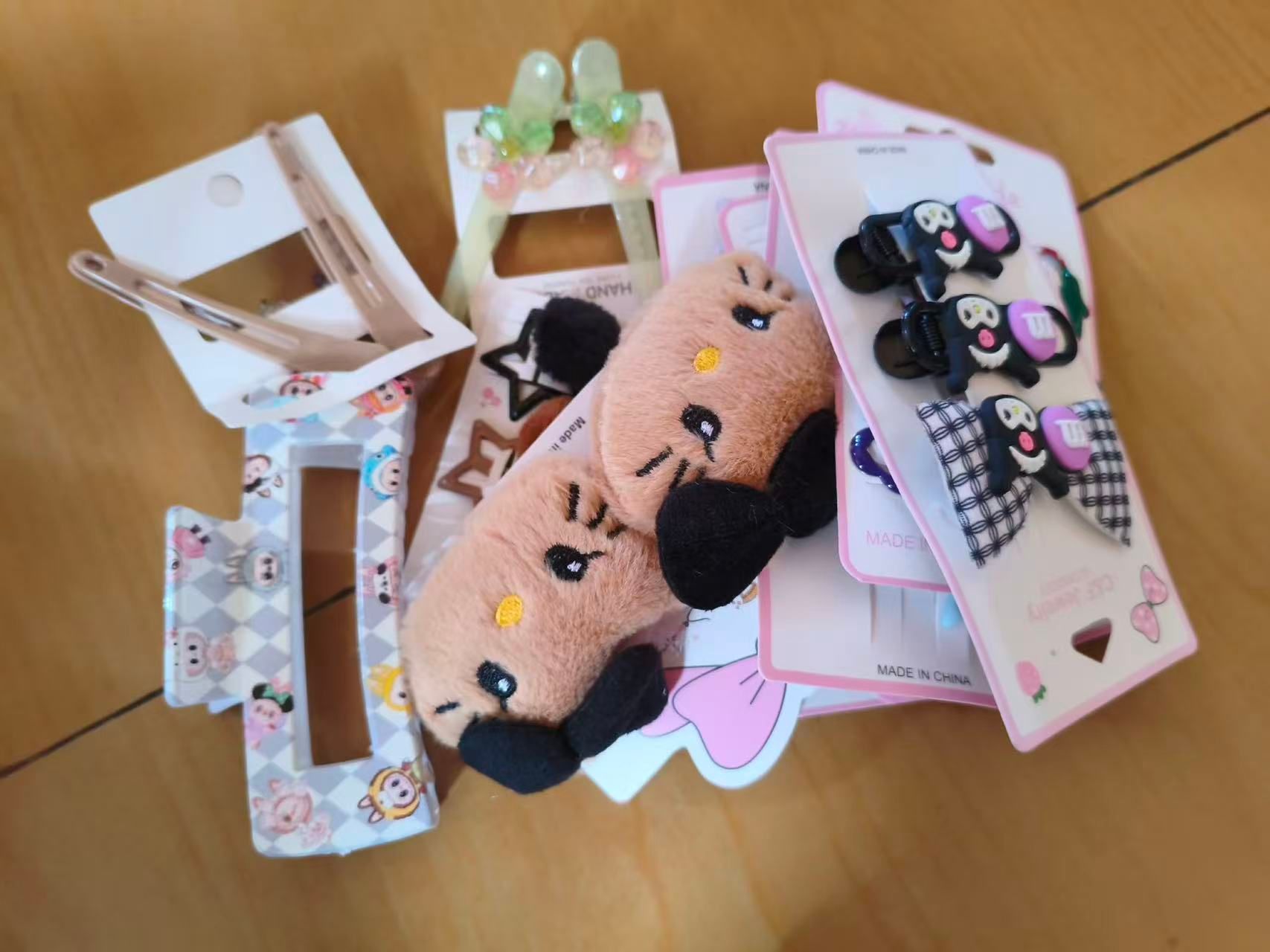 An assortment of hair clips and barrettes — including plush animal clips and carded sets — spread across a wooden floor.