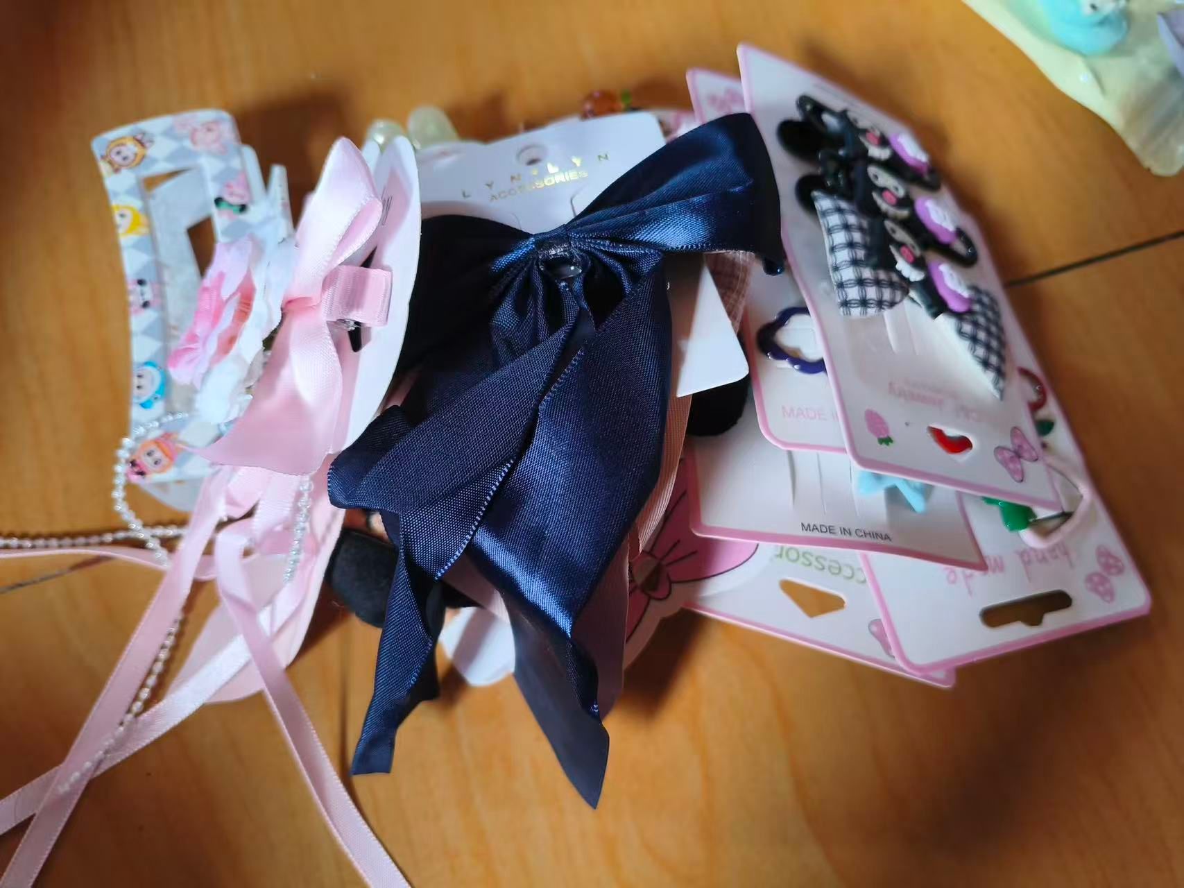A pile of hair accessories on a wooden floor: satin bows, ribboned clips and carded barrettes in pink, navy and patterned designs.
